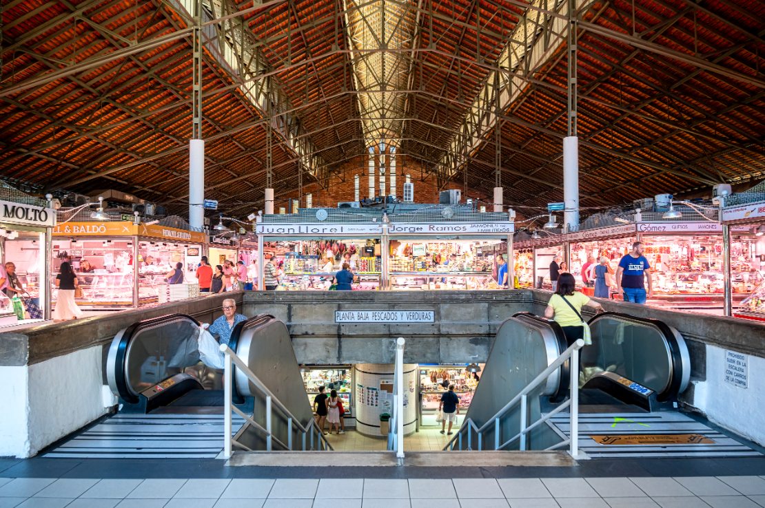 Mennesker på rulletrapp inne i Mercado Central i Alicante, med handlende i bakgrunnen.